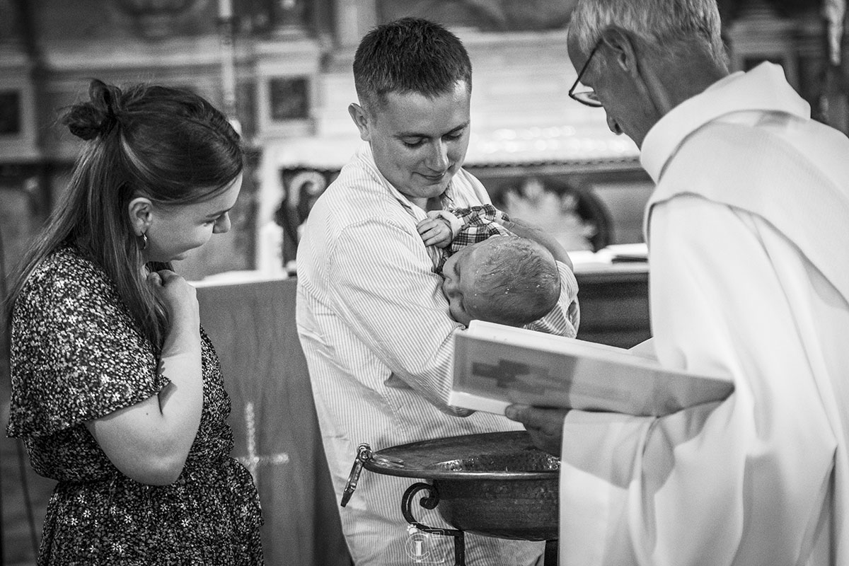 Photo en noir et blanc lors d'un batême en compagnie des parents, du bébé et du prêtre le baptisant