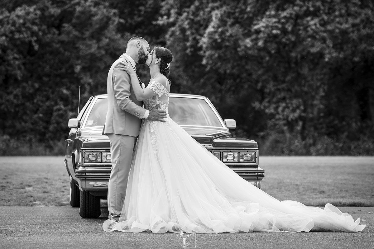 Photo des mariés s'embrassant devant une vieille voiture, noir et blanc