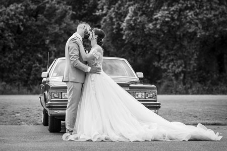 Photo des mariés s'embrassant devant une vieille voiture, noir et blanc