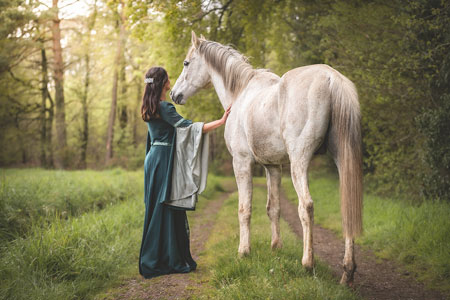 cavalière en robe verte a côté de son cheval arabe de dos dans un chemin