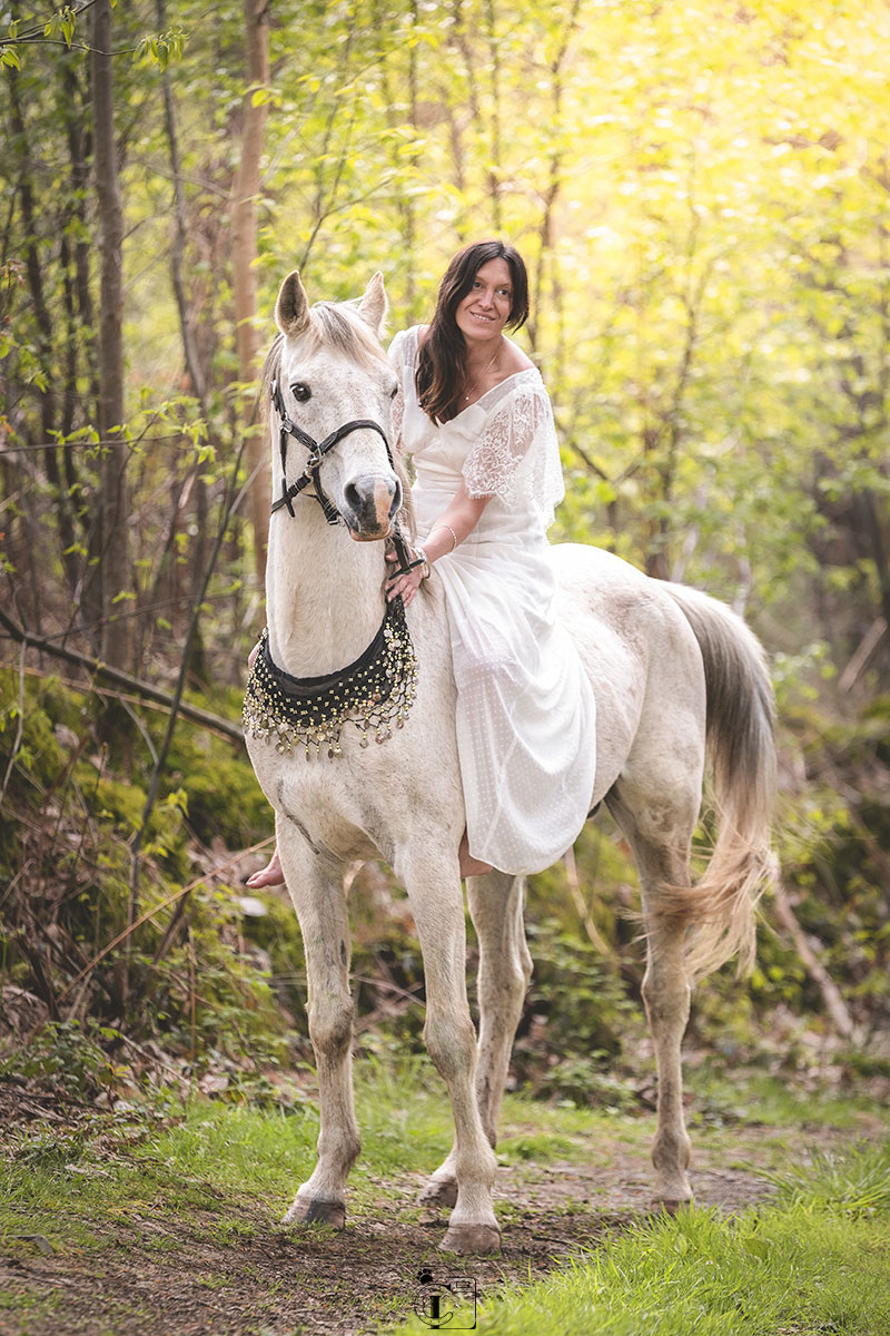 Cavalière en robe blanche sur son cheval arabe sur un chemin de fôret