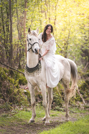 Cavalière en robe blanche sur son cheval arabe sur un chemin de fôret