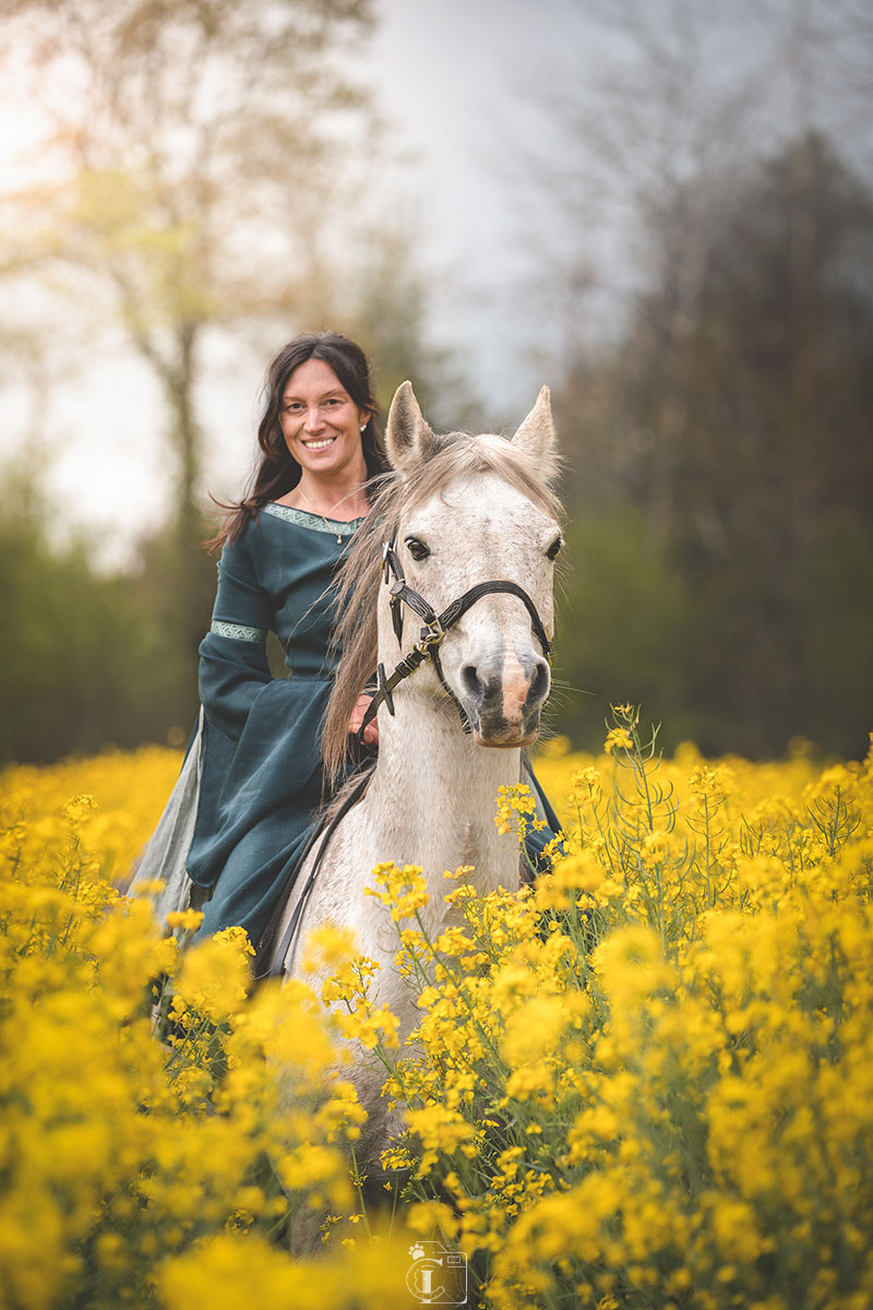 Cavalière en robe verte sur son cheval arabe dans un champ de colza