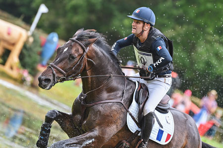 Cavalier français et son cheval marron entourés de gerbes d'eau lors du cross du Lion d'Angers