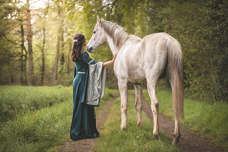 Photo d’une cavalière en robe verte du moyen-âge a côté de son cheval arabe